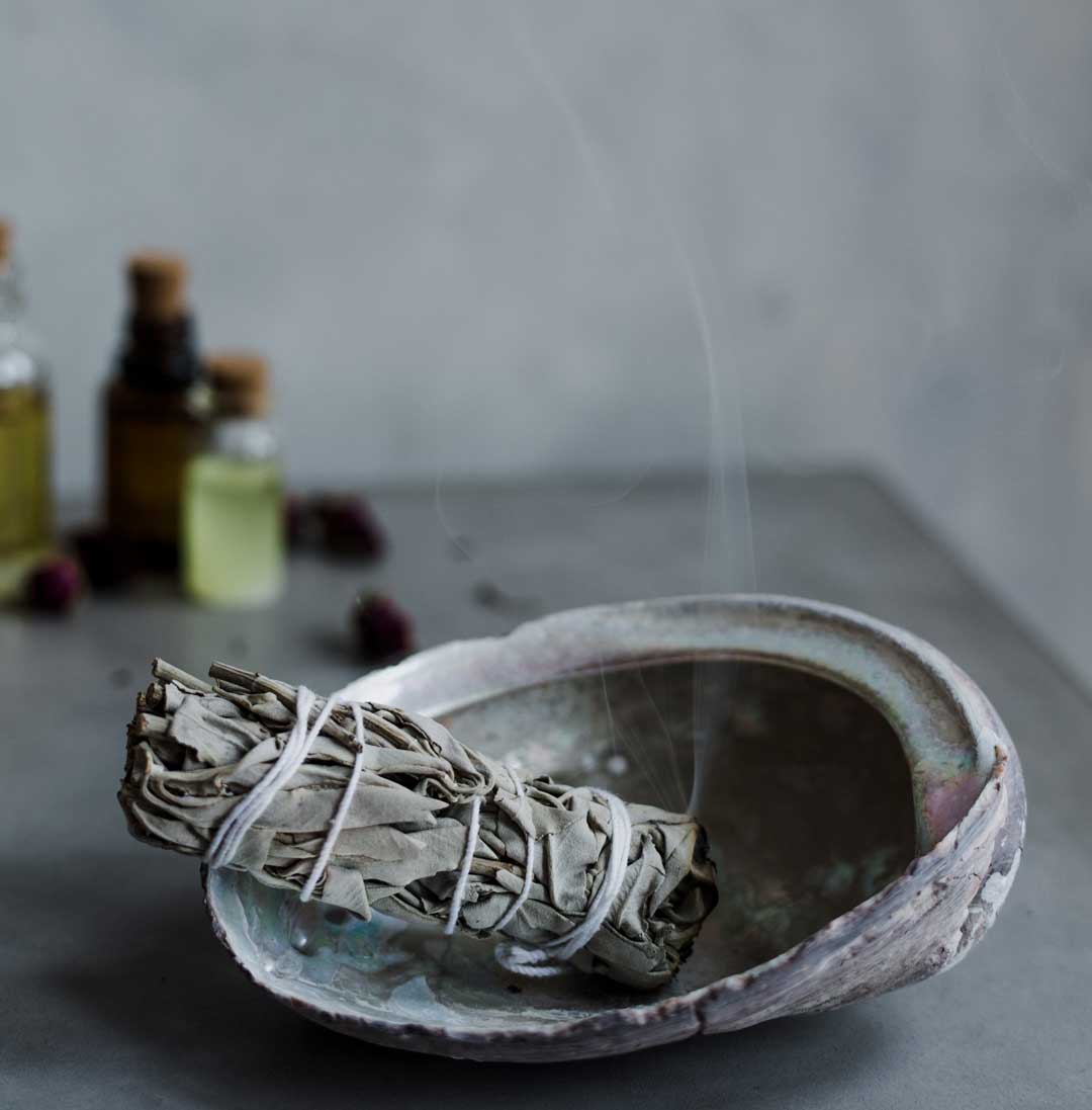 smudge stick smoking in a seashell ash tray with glass amber bottles of herbal medicine in background